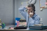 confused-employee-phone-office-desk-touching-his-head-46741238