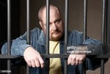 bald-mid-adult-man-standing-behind-prison-bars
