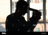 silhouette-of-young-man-with-gun-going-to-commit-suicide-near-window-TBANX1