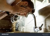 stock-photo-a-person-washing-their-face-in-a-bathroom-sink-with-water-splashing-2591916129