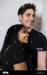 smiling-multiethnic-young-couple-with-black-clothes-looking-out-the-window-hugging-each-other-2EAYXDW