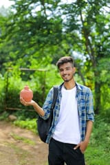 young-indian-college-boy-holding-clay-piggy-bank-hand-nature-background_75648-3214