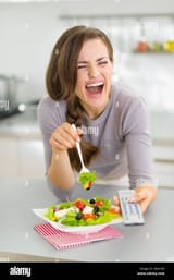 laughing-young-woman-eating-salad-and-watching-tv-in-kitchen-D6A1H0