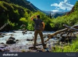 stock-photo-young-man-hiker-standing-in-a-mountain-gorge-near-river-and-looking-away-2334271837