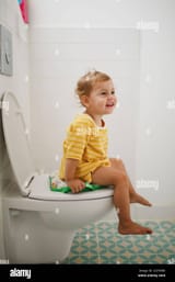 portrait-of-happy-girl-sitting-on-toilet-at-home-2GY9XBX