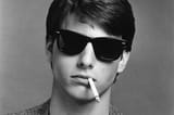 Greyscale-image-of-Tm-Cruise-wearing-black-80s-style-sunglasses-with-cigarette-hanging-out-his-mouth
