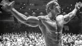 Arnold Schwarzenegger posing in the Mr. Olympia competition (1974) gray