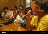 a-father-smokes-lit-cigarette-indoors-in-front-of-children-and-friends-AJC8DK