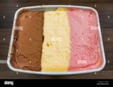 closeup-overhead-shot-of-a-fresh-tub-full-of-neapolitan-ice-cream-dessert-with-three-separate-layers-of-chocolate-vanilla-and-strawberry-flavours-TYKFB3