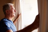 smiling-senior-white-man-opening-the-curtains-on-a-sunny-morning-side-view-close-up