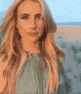 a woman in a green dress is standing on the beach laughing sticking her tongue out