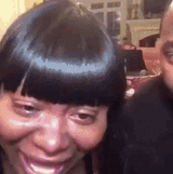 a woman with black hair is smiling while a man looks on
