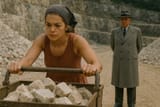Rita Ora pushes a cart full of rocks while Enver Hoxha watches