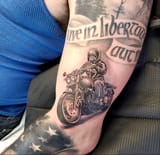 detailed-black-and-gray-motorcycle-tattoo-on-forearm-with-american-flag-elements-and-inspirational-banner-1384