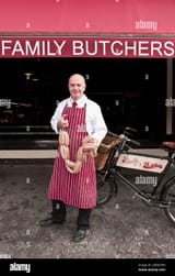 butcher-holding-sausage-in-front-of-his-shop-2BEN3PW