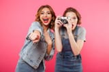 image-two-happy-ladies-friends-standing-isolated-over-pink-background-make-photo-camera-pointing-to-you-105867098-3686815736