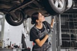 caucasian-mechanic-woman-fixing-underneath-car-auto-repair-shop-female-worker-grey-uniform-doing-vehicle-maintenance-repair-garage_1429-25860