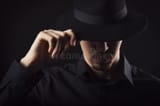 male-goatee-wearing-black-shirt-touching-his-fedora-hat-tipped-over-eyes-dark-background-tipping-close-up-173308673