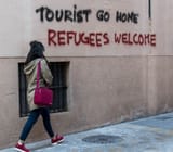 a-woman-walks-next-to-a-grafitti-that-reads-touris-1460627898697_rs