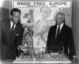 sarnoff-radio-free-europe-erik-hazelhoff - Two men in suits look at a model of a radio tower in front of a map