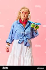 hipster-vibe-senior-beautiful-woman-in-stylish-casual-clothes-shirt-skirt-and-sunglasses-posing-with-skateboard-over-pink-studio-background-2T0W7D3