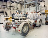 ap15-KSC-71PC-310HR - Dave Scott (yellow arm bands, center) and Jim Irwin (yellow arm bands, right) examine the frontend of the flight Rover - 8 April 1971