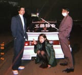 2 guys standing 1 girl sitting