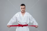 graphicstock-picture-of-sportsman-dressed-in-kimono-practice-in-karate-while-tightening-red-belt-isolated-over-grey-background-look-at-camera_BuwSNsU2g_SB_PM
