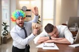 166762799-young-man-popping-paper-bag-behind-his-sleeping-colleague-in-office-funny-joke