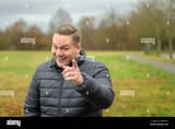 amused-young-man-pointing-at-camera-wuth-knowing-look-as-he-stands-in-a-park-in-autumn-in-a-warm-thick-jacket-2HBRTYF