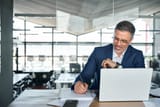 mid-aged-business-man-working-on-laptop-computer-in-office-writing-notes[1]