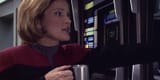 captain-janeway-kate-mulgrew-with-a-cup-of-coffee-looks-at-a-wall-panel-voyager