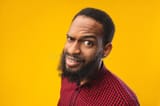 confused-african-american-man-looking-camera-close-up-headshot-raised-eyebrow-yellow-studio-wall-184093449