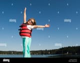 a-young-girl-in-a-life-jacket-joyfully-raises-her-arms-while-playing-BE27JN