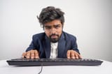 indian-man-glasses-working-computer-his-hands-hover-keyboard-while-typing-isolated-white-background-front-view_621325-1874