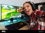 excited-girl-gamer-sitting-at-the-table-playing-online-games-on-a-computer-indoors-taking-a-selfie-RBP35B