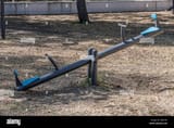 metal-seesaw-on-dirt-floor-children-outdoor-recreation-area-in-a-public-park-tree-trunk-and-shadows-in-blurred-background-sunny-day-in-mexico-2PJ61A9[1]
