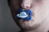 unshaven-young-man-holding-pacifier-his-mouth-bristle-blue-120799181