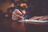 midsection-man-holding-pen-book-table_1048944-10463449
