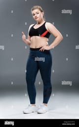 beautiful-overweight-girl-in-sportswear-showing-thumb-up-and-looking-at-camera-on-grey-R1YF13