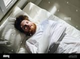 above-angle-of-young-bearded-man-in-straitjacket-suffering-from-schizophrenia-lying-on-bed-in-ward-of-mental-hospital-2R86JP8