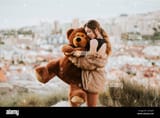 woman-with-eyes-closed-hugging-teddy-bear-while-standing-against-city-2CCKJ4Y